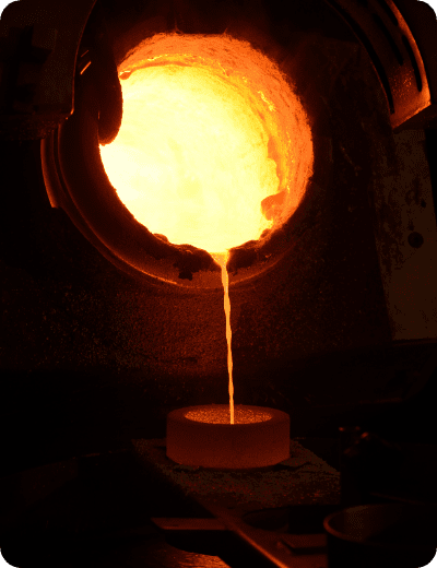 Metallo fuso di colore arancione brillante viene versato da una fornace in uno stampo circolare in un ambiente industriale buio.