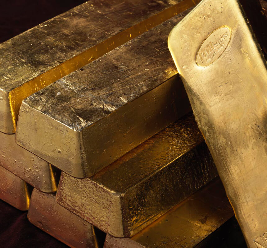 Una vista ravvicinata di lingotti d'oro impilati, con un lingotto appoggiato agli altri, che mostrano una superficie lucida e metallica e una struttura visibile.