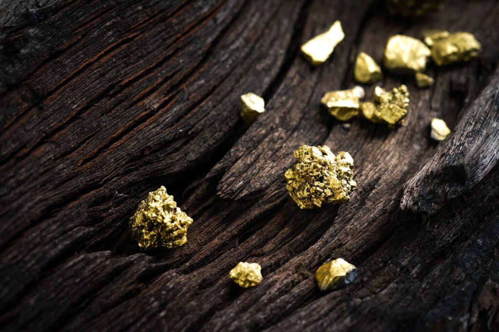 Piccole pepite e frammenti d'oro sparsi su una superficie di legno ruvida e scura.