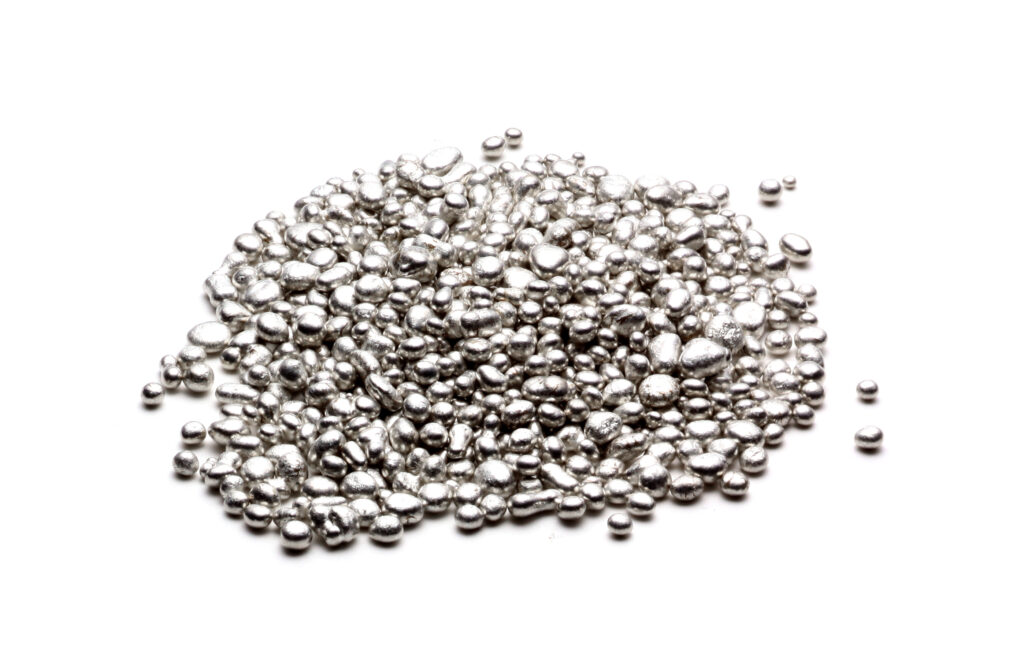Un mucchio di piccole palline metalliche argentate e lucide sparse su uno sfondo bianco.
