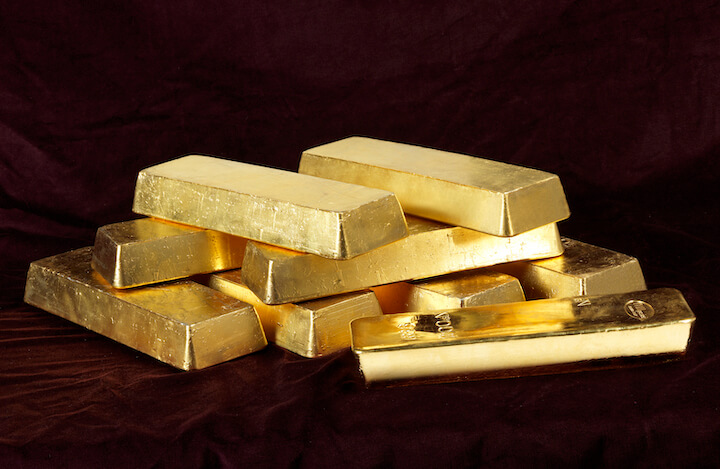 Una pila di lingotti d'oro lucidi è disposta su una superficie marrone scuro, riflettendo la luce e mettendo in evidenza la loro lucentezza metallica.