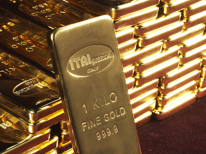 Primo piano di un lingotto d'oro da 1 chilogrammo marcato ITALPREZIOSI 1 KILO FINE GOLD 999.9 in piedi davanti a una pila di lingotti d'oro simili, tutti splendenti di una brillante tonalità dorata.