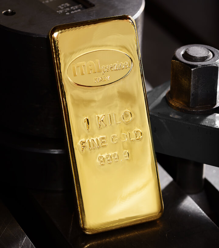 Un lingotto d'oro lucido da 1 chilogrammo con l'incisione ITALpreziosi ITALY 1 KILO FINE GOLD 999.9, appoggiato su un macchinario metallico industriale.