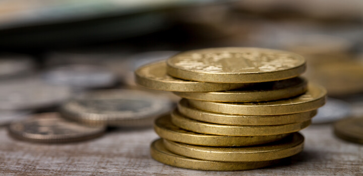 Primo piano di pile di monete d'oro su una superficie di legno, con altre monete sfocate sullo sfondo.