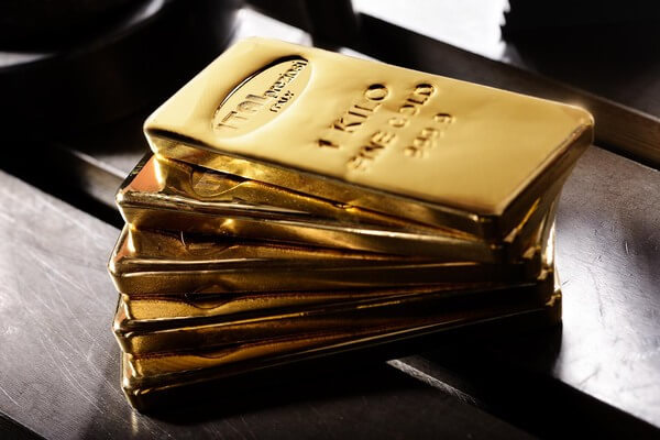 Una pila di lingotti d'oro lucidi con l'etichetta 1 KILO FINE GOLD 999.9 poggia su una superficie metallica, riflettendo la luce.