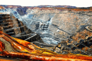 Una grande miniera a cielo aperto con ripide pareti di roccia terrazzate e strade tortuose che scendono nel pozzo. La terra esposta mostra strati di tonalità rosse, arancioni e grigie sotto un cielo luminoso.