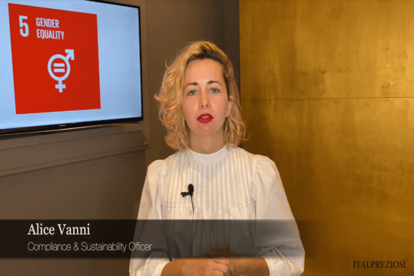 Una donna dai capelli ricci e biondi parla davanti a una parete dorata. Il testo sullo schermo recita Alice Vanni, Compliance Sustainability Officer. Un monitor visualizza 5 Gender Equality con un simbolo grafico di genere.