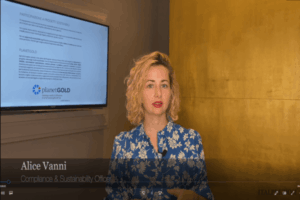 Una donna con i capelli ricci e biondi, che indossa una camicetta blu a fiori, parla davanti a un televisore che mostra una diapositiva di presentazione. Il testo in basso recita Alice Vanni, Compliance Sustainability Officer.