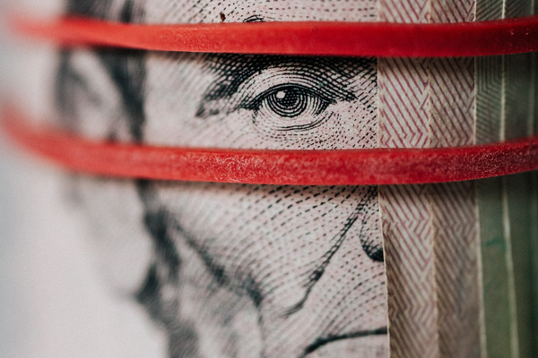 Primo piano di una banconota statunitense arrotolata e fissata con elastici rossi, con particolare attenzione a un occhio dettagliato di un ritratto sulla banconota.