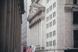 Veduta dell'edificio della Borsa di New York con le sue alte colonne, le bandiere americane esposte davanti e gli edifici in pietra circostanti nel Financial District di New York.