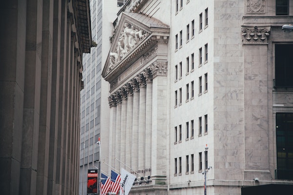 Veduta dell'edificio della Borsa di New York con le sue alte colonne, le bandiere americane esposte davanti e gli edifici in pietra circostanti nel Financial District di New York.