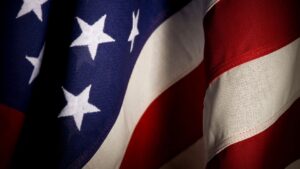 Primo piano della bandiera degli Stati Uniti che mostra stelle bianche in campo blu e strisce rosse e bianche, con pieghe del tessuto che creano ombre e luci.