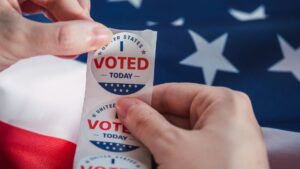Una persona stacca l'adesivo I Voted Today, con la bandiera degli Stati Uniti con stelle bianche su sfondo blu visibile sotto.