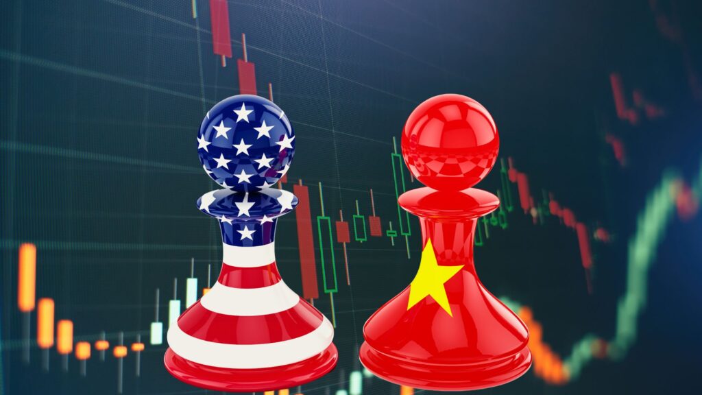 Two chess pawns, one with a U.S. flag design and the other with a Chinese flag design, stand in front of a stock market chart with red and green candlesticks.
