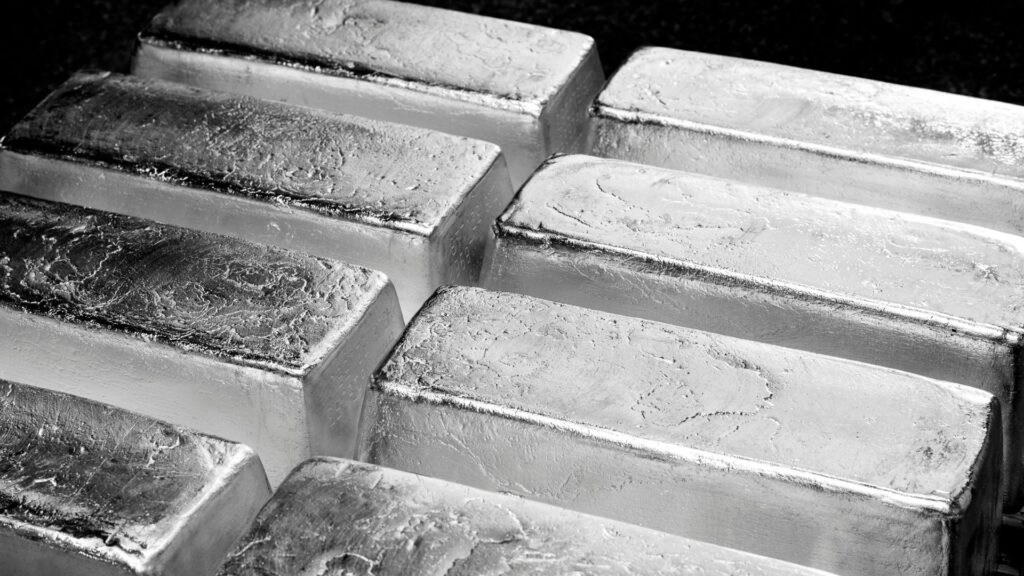 A close-up of several shiny silver bars stacked together, showing their textured surfaces and metallic sheen.