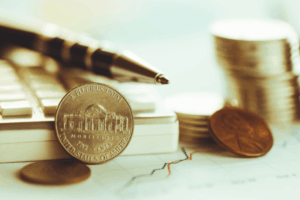 Primo piano di monete americane, una penna e una calcolatrice su un grafico finanziario con linee, che rappresenta la pianificazione finanziaria e la contabilità.