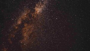 Un denso ammasso di stelle nel cielo notturno, che mostra una parte della galassia della Via Lattea con aree luminose di colore arancione e innumerevoli piccole stelle sparse su uno sfondo scuro.