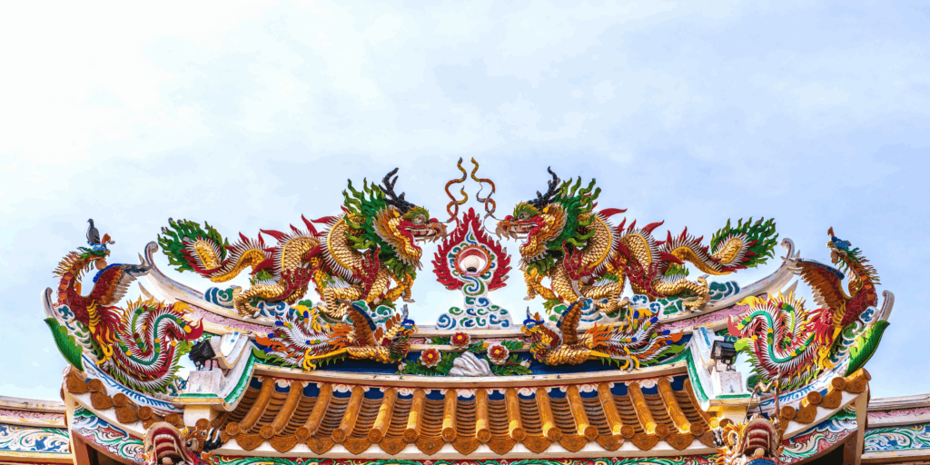 Draghi dai colori vivaci e motivi intricati decorano il tetto ornato di un tempio cinese tradizionale contro un cielo blu, mostrando rossi, verdi, gialli e blu vibranti in intagli e disegni dettagliati.