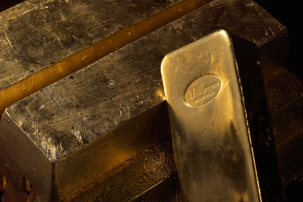 Primo piano di diversi lingotti d'oro impilati tra loro, con un lingotto in primo piano che presenta un marchio stampato e riflessi che ne evidenziano la superficie lucida e metallica.