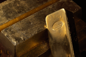 Primo piano di diversi lingotti d'oro impilati tra loro, con un lingotto in primo piano che presenta un marchio stampato e riflessi che ne evidenziano la superficie lucida e metallica.