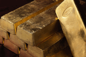 Una pila di lingotti d'oro lucidi è disposta su una superficie scura, con un lingotto d'oro appoggiato alla pila, che mostra un marchio impresso sulla sua superficie.