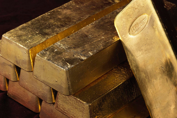 Una pila di lingotti d'oro lucidi è disposta su una superficie scura, con un lingotto d'oro appoggiato alla pila, che mostra un marchio impresso sulla sua superficie.