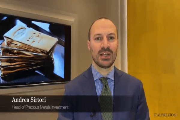 Un uomo in giacca e cravatta si trova di fronte a una parete gialla e a un televisore che mostra lingotti d'oro. Il testo dell'immagine recita: Andrea Sirtori, Responsabile Investimenti Metalli Preziosi. Il logo ITALPREZIOSI appare nell'angolo in basso a destra.