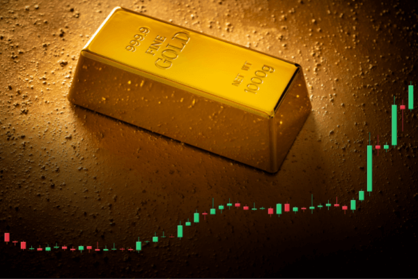 Un lingotto d'oro con la dicitura 999.9 FINE GOLD 1000g si trova su una superficie d'oro testurizzata, con un grafico a candele ascendente sovrapposto, che rappresenta l'aumento del prezzo dell'oro.