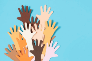 Ritagli di carta di mani di varie tonalità di pelle sono sollevati insieme su uno sfondo blu, a simboleggiare la diversità, l'inclusione e l'unità.