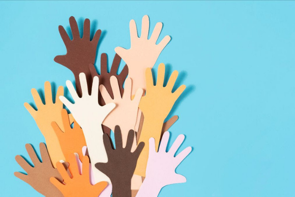 Ritagli di carta di mani di varie tonalità di pelle sono sollevati insieme su uno sfondo blu, a simboleggiare la diversità, l'inclusione e l'unità.