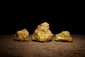 Tre pepite d'oro di varie dimensioni sono esposte su una superficie ruvida e marrone su uno sfondo scuro e nero.