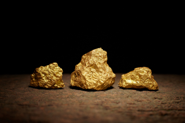 Tre pepite d'oro di varie dimensioni sono esposte su una superficie ruvida e marrone su uno sfondo scuro e nero.