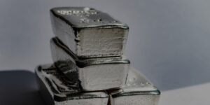 Tre barre d'argento sono impilate in modo irregolare su uno sfondo chiaro, con texture e segni visibili sulla superficie delle barre.