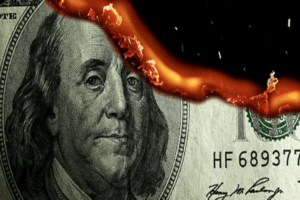 Un primo piano di una banconota da 100 dollari USA con il bordo superiore in fiamme, che mostra fiamme e braci che consumano parte della banconota.