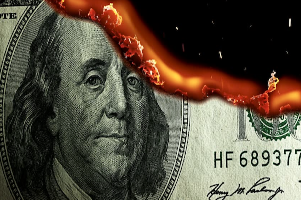 Un primo piano di una banconota da 100 dollari USA con il bordo superiore in fiamme, che mostra fiamme e braci che consumano parte della banconota.