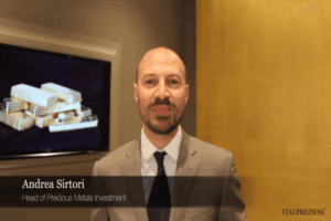 Un uomo in giacca e cravatta sta in casa e sorride alla telecamera. Dietro di lui c'è un'immagine incorniciata di lingotti d'oro. Il testo recita: Andrea Sirtori, Responsabile Investimenti Metalli Preziosi e ITALPREZIOSI nell'angolo.