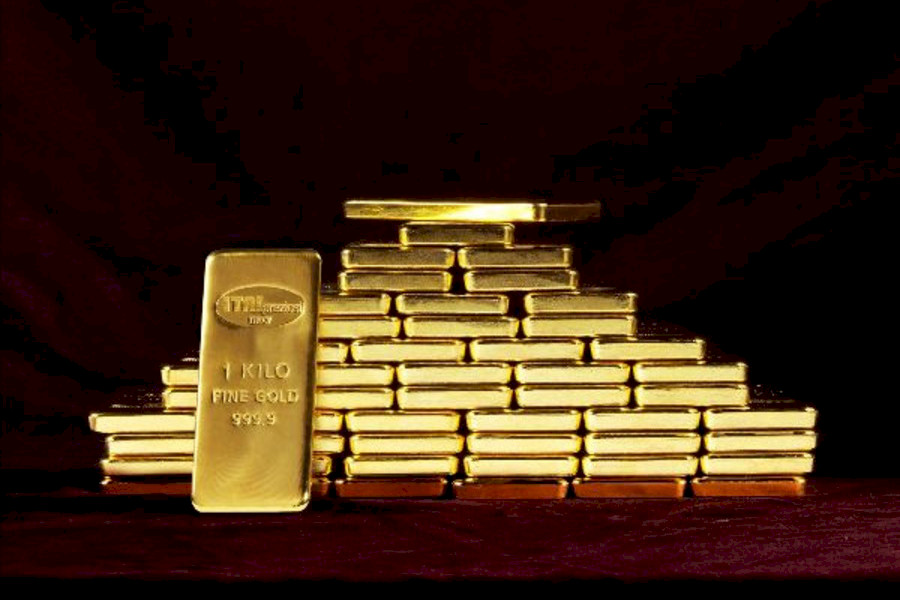 Una pila piramidale di lingotti d'oro su sfondo scuro, con un lingotto d'oro grande contrassegnato da 1 KILO FINE GOLD 999.9 in piedi davanti alla pila.