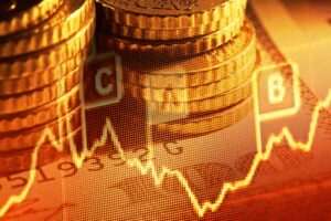 Sullo sfondo sono raffigurate pile di monete con un grafico finanziario sovrapposto, caratterizzato da un grafico a linee fluttuanti e da simboli di valuta, che simboleggiano la crescita economica e i mercati finanziari.