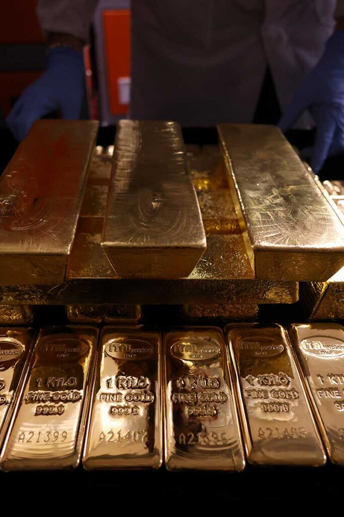 Lingotti d’oro marchiati Italpreziosi disposti su un tavolo, con una persona che indossa guanti blu che li maneggia