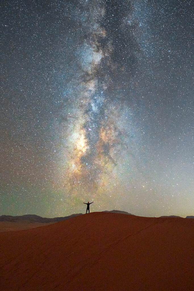 Persona su una duna osserva la Via Lattea in un cielo stellato, simbolo di connessione tra uomo e universo